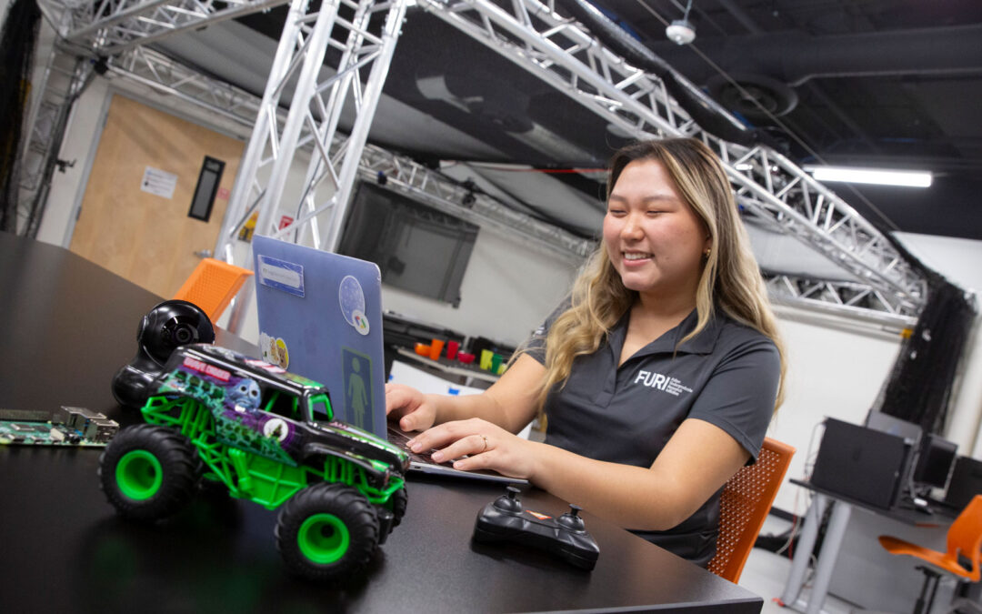 A student types on laptop and works with a robotic car.